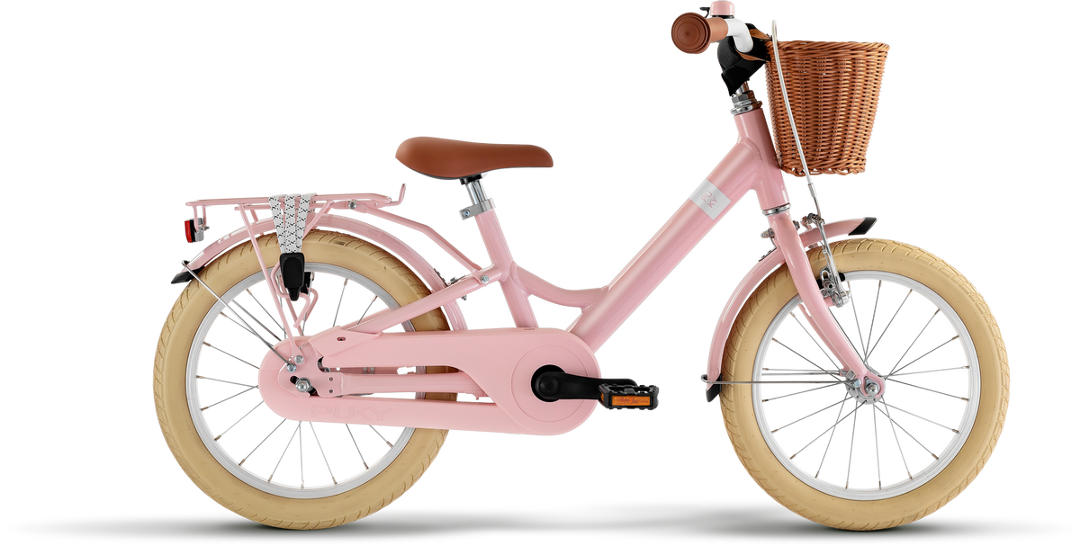 PUKY YOUKE CLASSIC 16 är en rosa barncykel med beige däck, brun sadel och handtag, lättviktsram i aluminium, flätad korg fram och pakethållare bak med vit elastisk rem, som visas på en vit bakgrund.