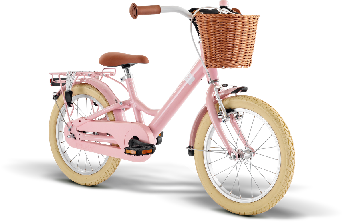 PUKY YOUKE CLASSIC 16, en rosa barncykel med lättviktsram i aluminium, cremefärgade däck, brun sadel och styre, flätad korg fram och silverfärgat pakethållare bak, visas mot en vit bakgrund.