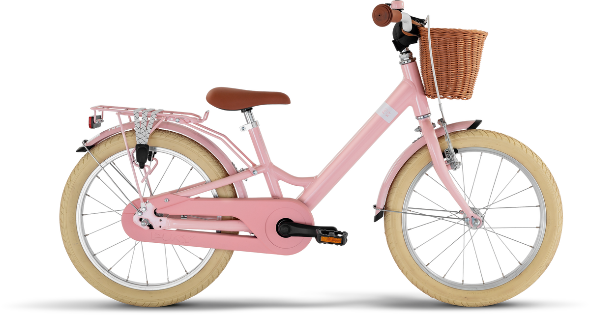 PUKY YOUKE CLASSIC 18 är en rosa barncykel med gräddfärgade däck, brun sadel och styre, flätad korg fram och pakethållare bak, mot en vit bakgrund.