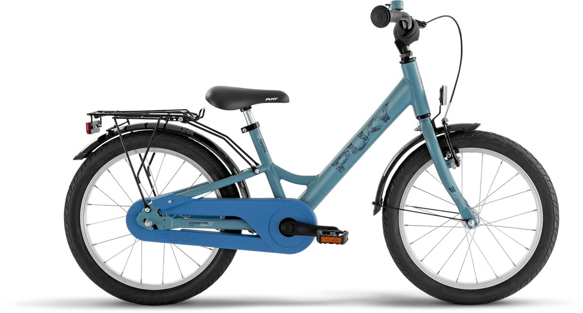 PUKY YOUKE 18 är en blå barncykel med svart sadel, svart styre, främre och bakre stänkskärmar, bakre lasthållare och kedjeskydd, mot en vit bakgrund.