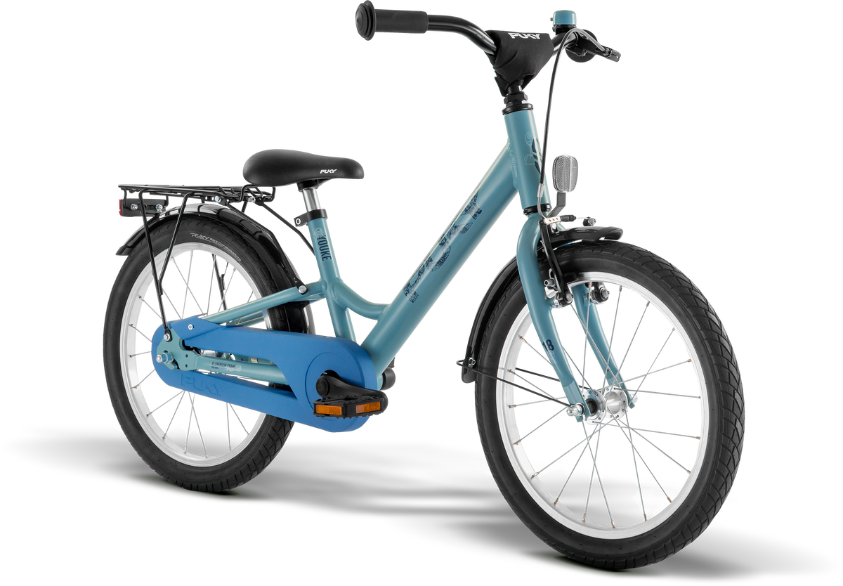 PUKY YOUKE 18 är en blå barncykel med svart sadel och styre, stänkskärmar fram och bak, lasthållare bak, pedalreflektorer, mot en vit bakgrund.