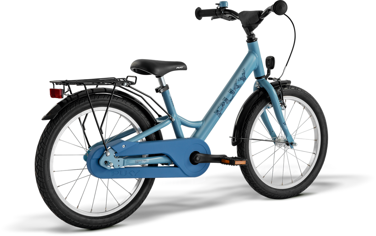 PUKY YOUKE 18 är en blå barncykel med svart sadel, svart styre, pakethållare bak, kedjeskydd, pedal- och bakreflektorer samt tjocka däck.