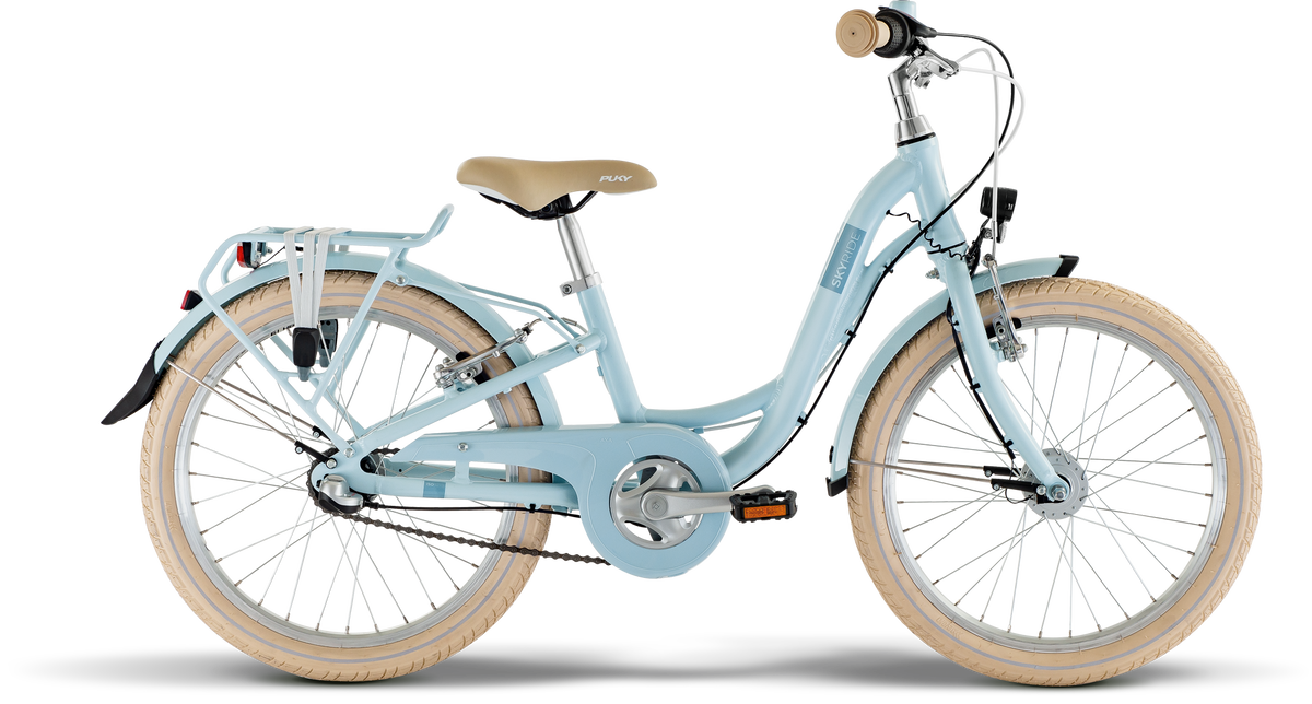 PUKY SKYRIDE 20-3 är en ljusblå barncykel med beige sadel och styre, cremefärgade däck, pakethållare bak, skärmar och kedjeskydd, mot en vit bakgrund.