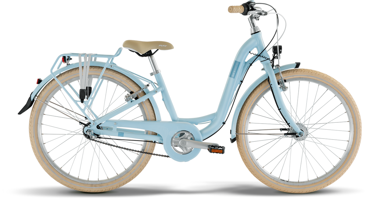 PUKY SKYRIDE 24-3 är en ljusblå genomgångscykel med beige däck och sadel, upprätt styre, pakethållare, fram- och bakskärmar, som visas mot en vit bakgrund.