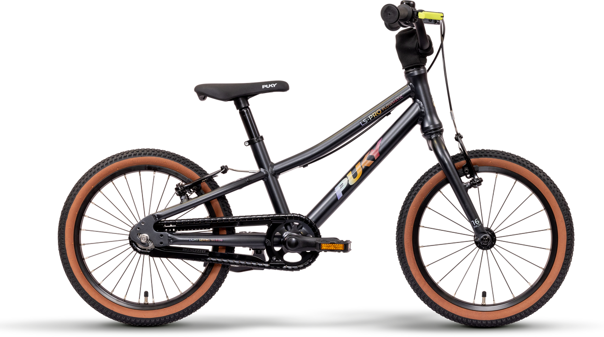 En svart PUKY LS PRO 16-2 FLOWMATIC barncykel med bruna däck, svart sadel och rakt styre, sedd från sidan mot en vit bakgrund. "PUKY" står med färgglada bokstäver på ramen.