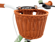 Närbild av ett ljusgrönt cykelstyre med bruna handtag och en korg CHAOS KORB - L framtill, som hålls fast med bruna läderremmar. Varumärket PUKY syns på ramen bakom korgen.